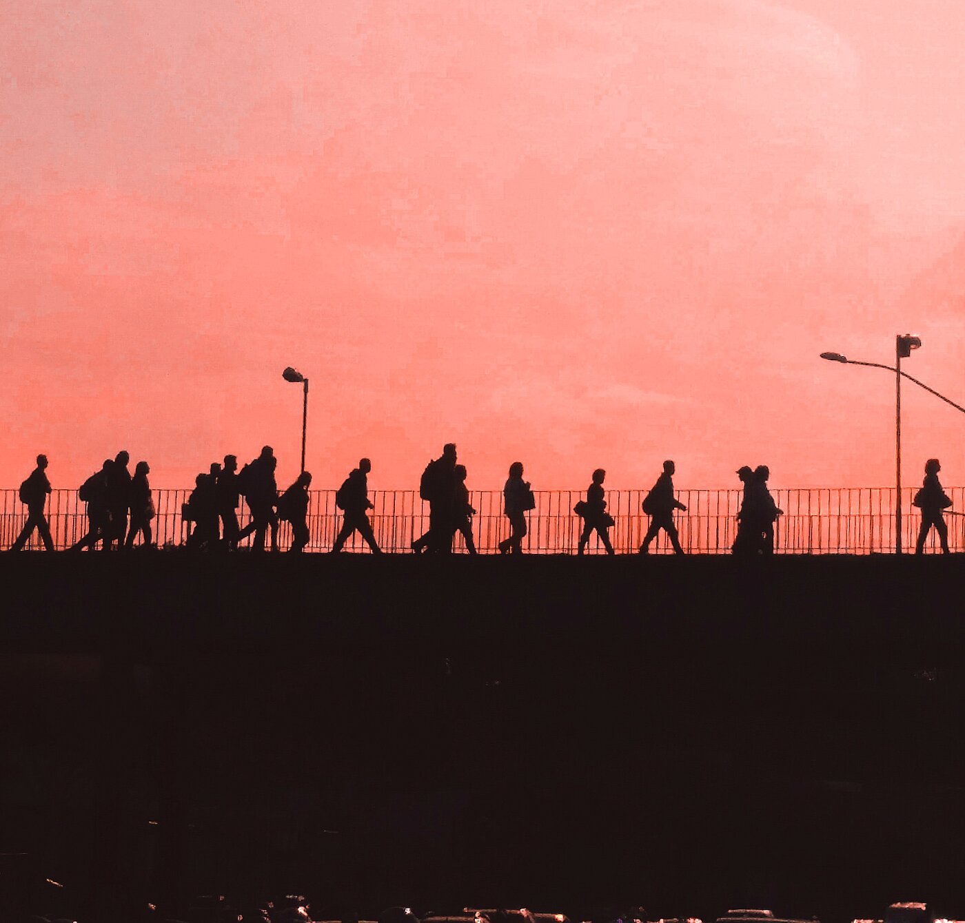 Das Bild zeigt Menschen, die mit Gepäck eine Straße im Gegenlicht einer untergehenden Sonne entlang gehen