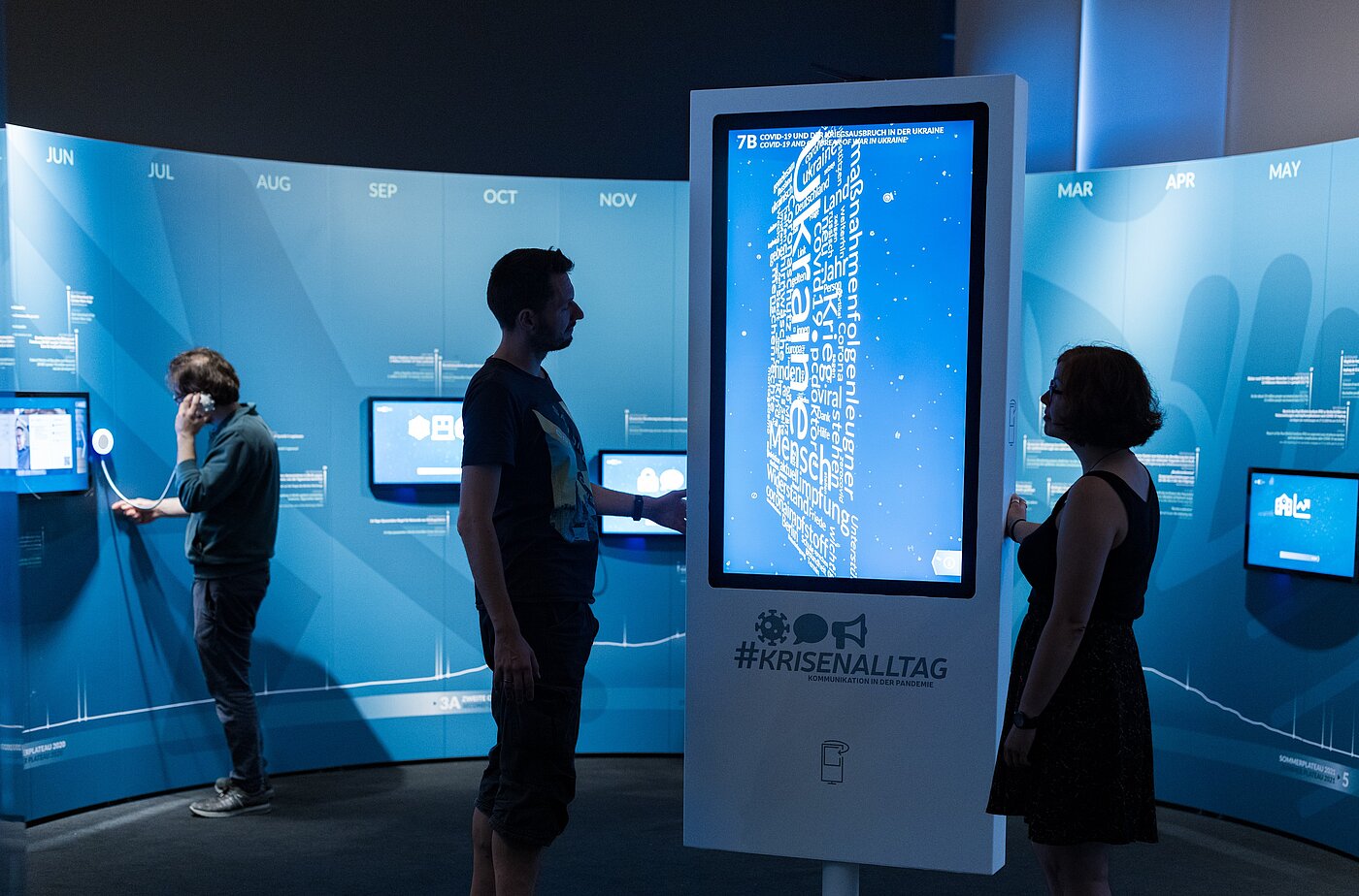 Das Bild zeigt Menschen in einer Ausstellung vor einem großen Bildschirm