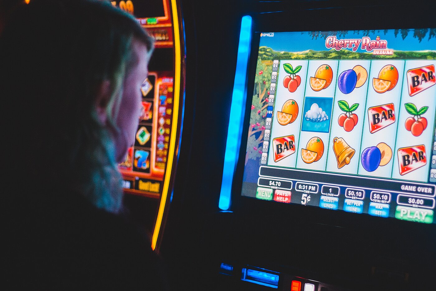 Das Bild zeigt einen Menschen, der vor einem Glücksspielautomaten sitzt