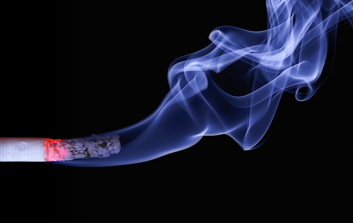 brennende Zigarette vor schwarzem Hintergrund mit blauem Rauch