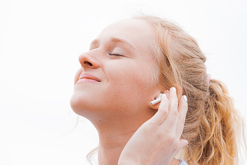 Foto einer jungen Frau, die mit geschlossenen Augen Podcasts über Kopfhörer genießt